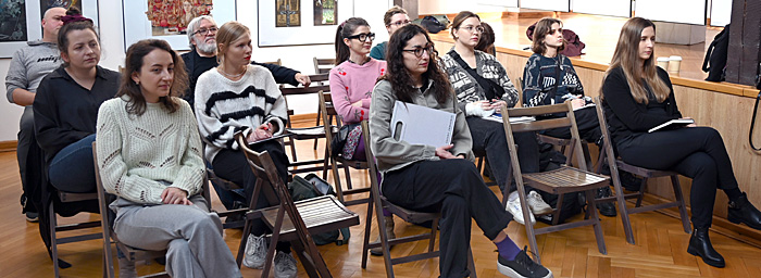 Uczestnicy warsztatów siedzą w Galerii i słuchają wykładu. 