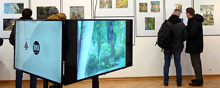 Miłośnicy sztuki na otwarciu Festiwalu Ilustracji Polskiej oglądają ilustracje. Na ekranach monitorów widoczne animacje powstałe podczas warsztatów. 